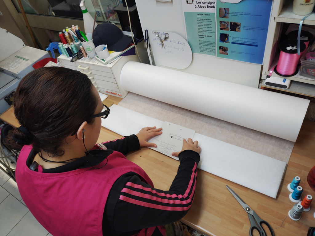 Jeune adulte préparant un support de broderie sur un plan de travail dans le cadre du SESSAD Pro insertion professionnelle