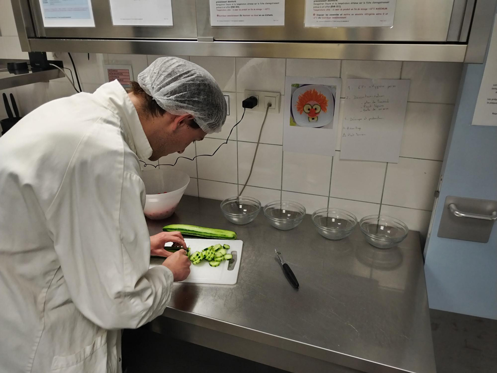 Jeune adulte en stage en cuisine préparant et découpant des légumes dans le cadre du SESSAD Pro insertion professionnelle