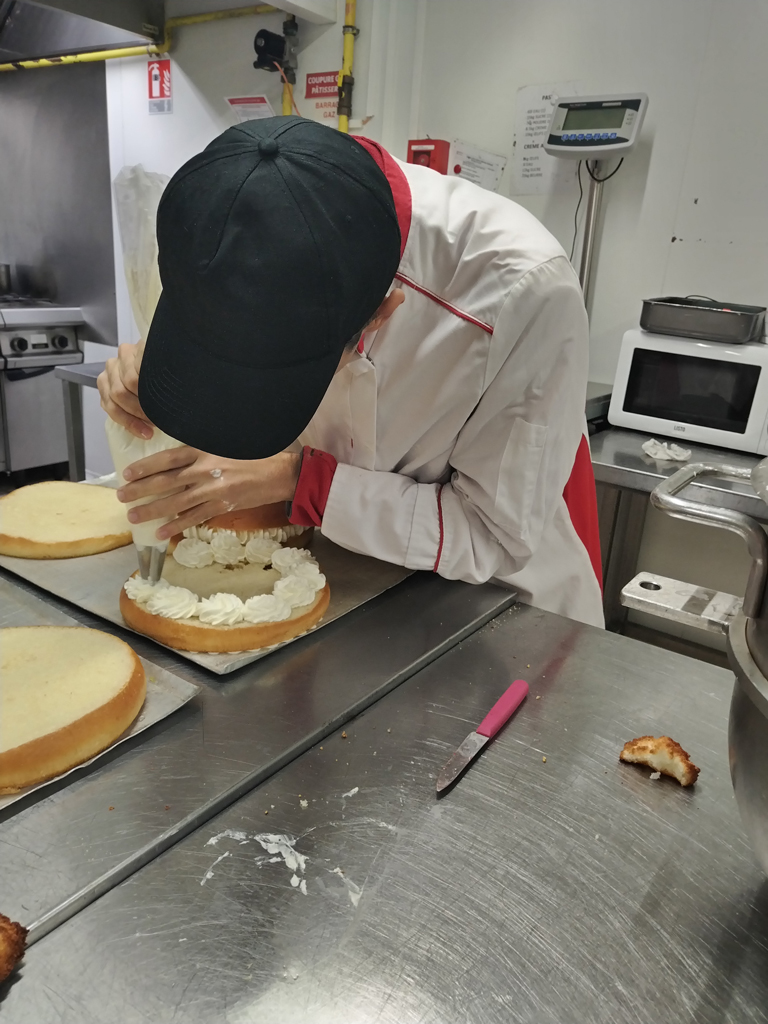 Jeune adulte réalisant la préparation d’un gâteau en stage en pâtisserie chez Auchan dans le cadre du SESSAD Pro insertion professionnelle